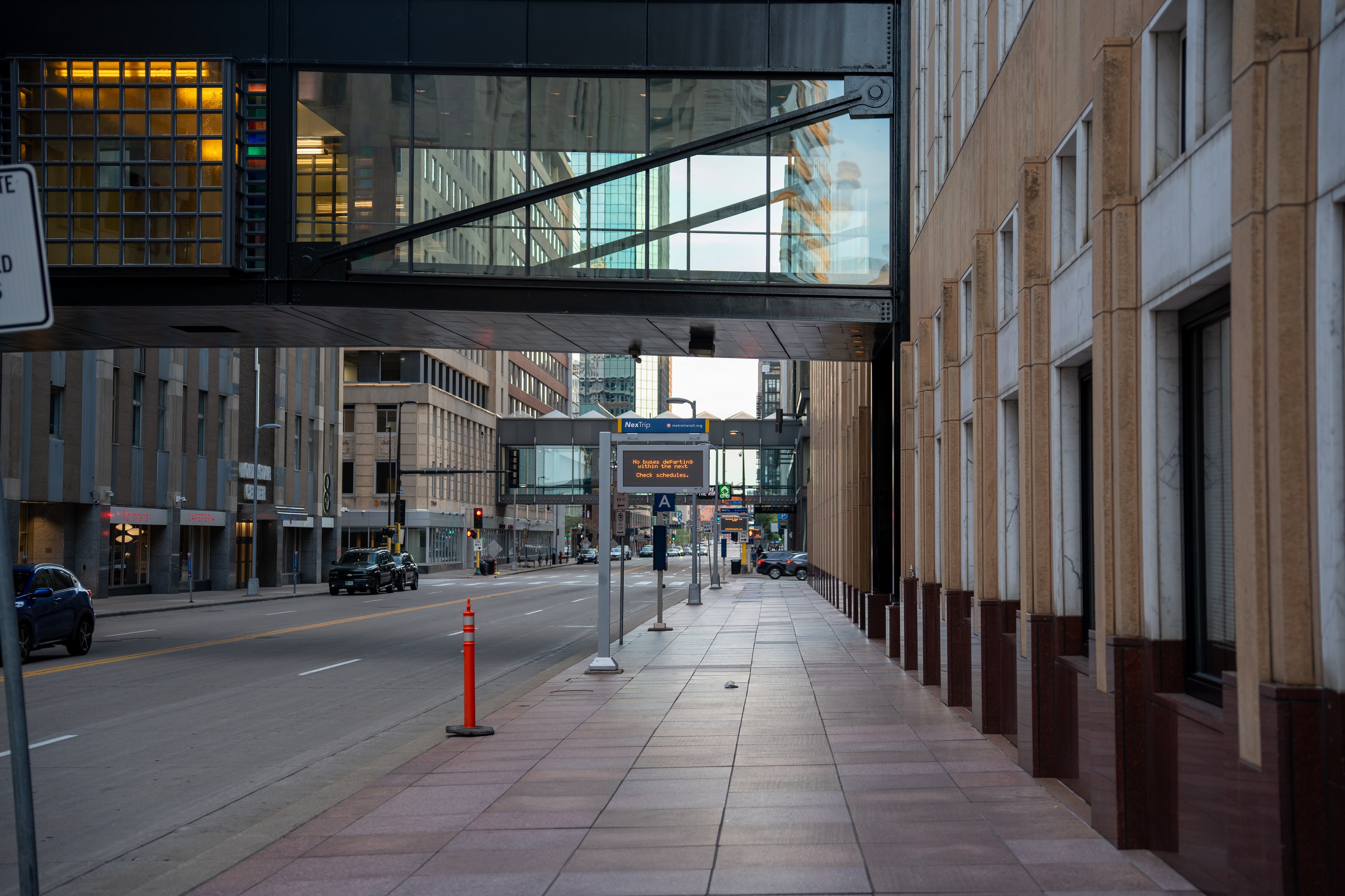 An empty sidewalk running beneath a lit skyway, with traffic cones and a distant illuminated sign.