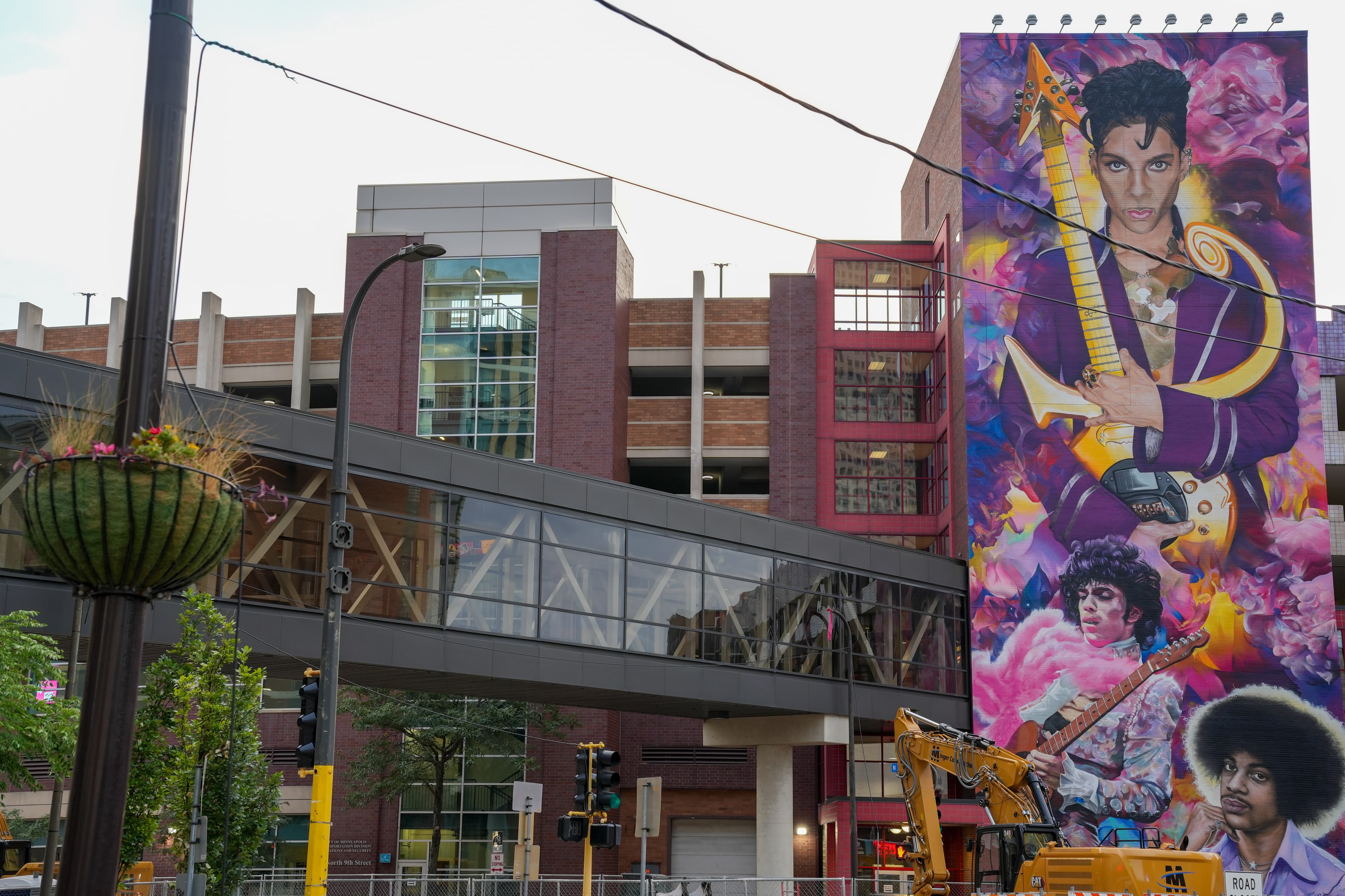A tall painted mural of Prince rising beside a concrete parking ramp and an overhead skyway.