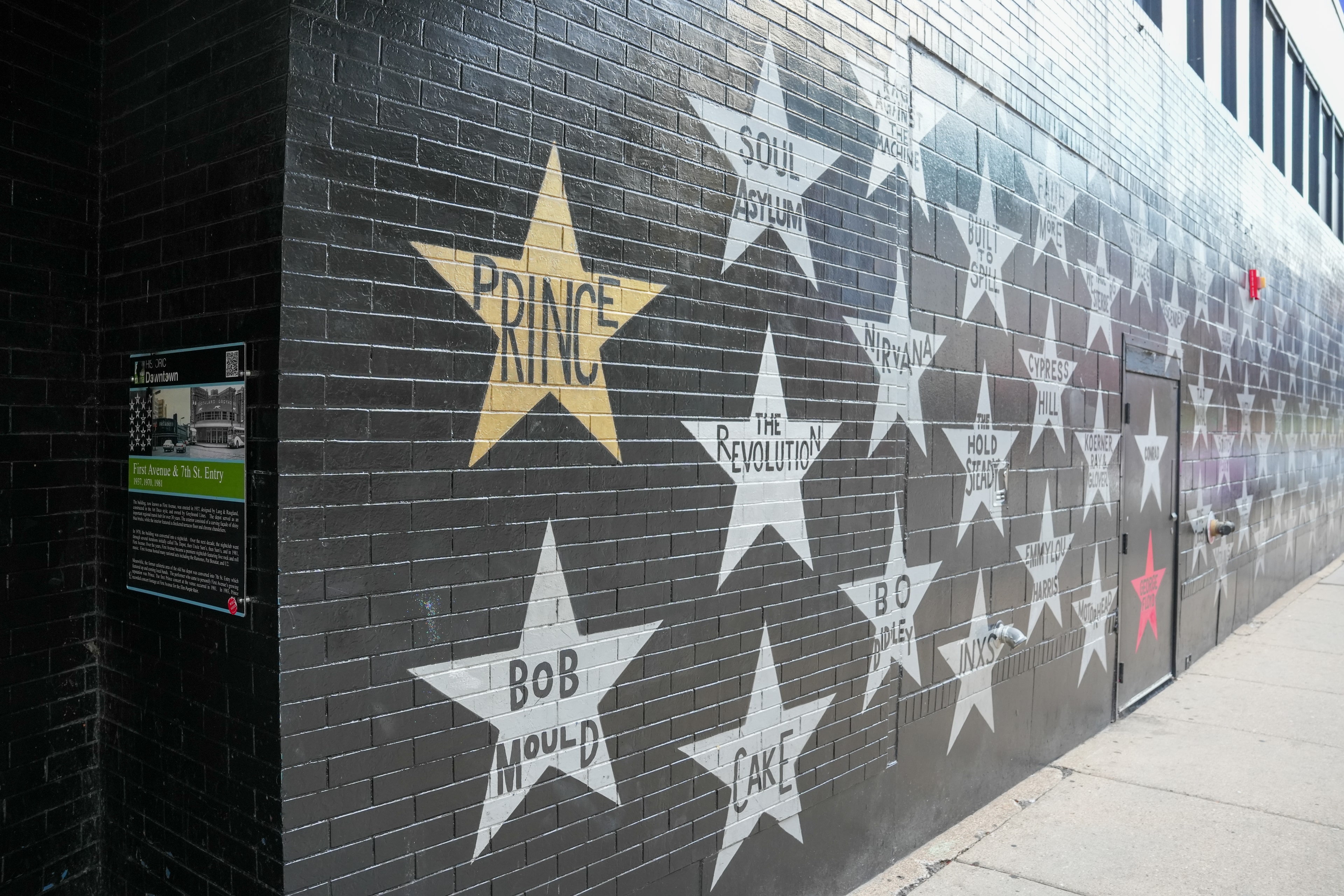 Painted silver and gold stars bearing musicians' names across a black-painted brick wall.
